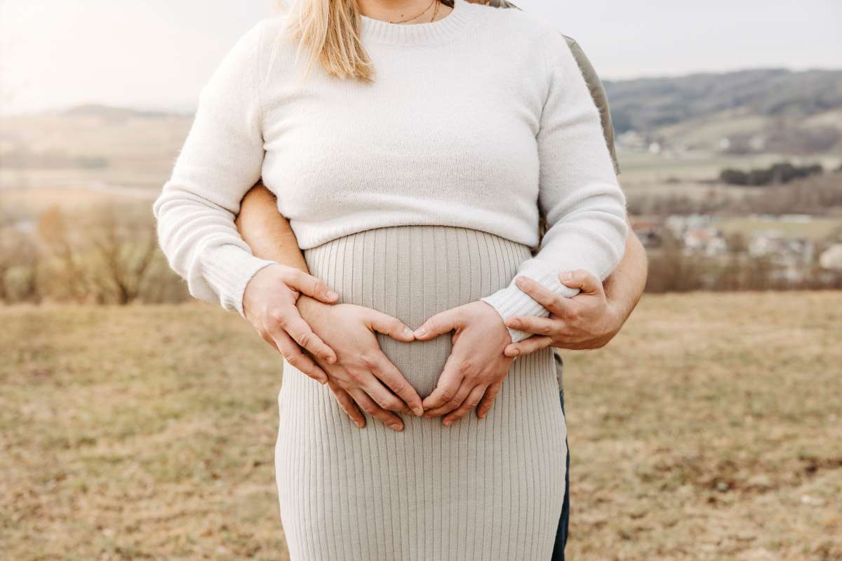 Schwangere und ihr Partner formen mit den H&auml;nden ein Herz auf dem Babybauch
