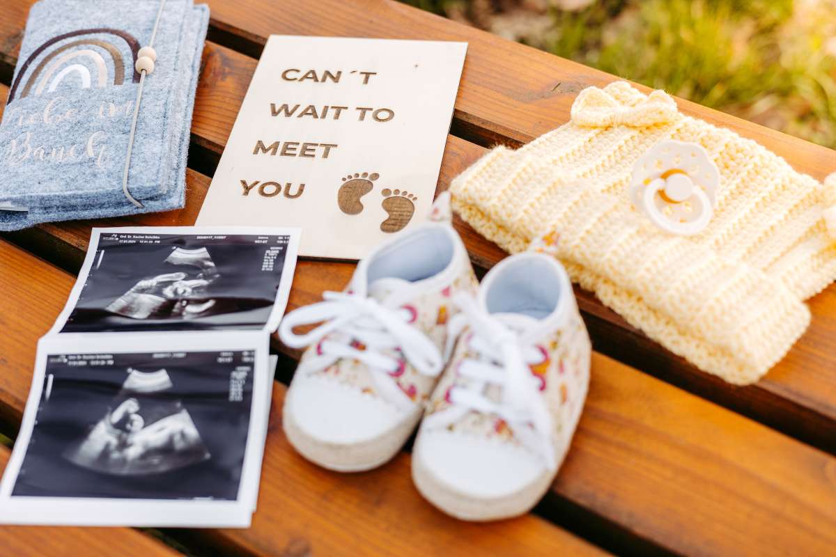 Babyschuhe, Ultraschallbilder und eine Strickm&uuml;tze auf einer Holzbank