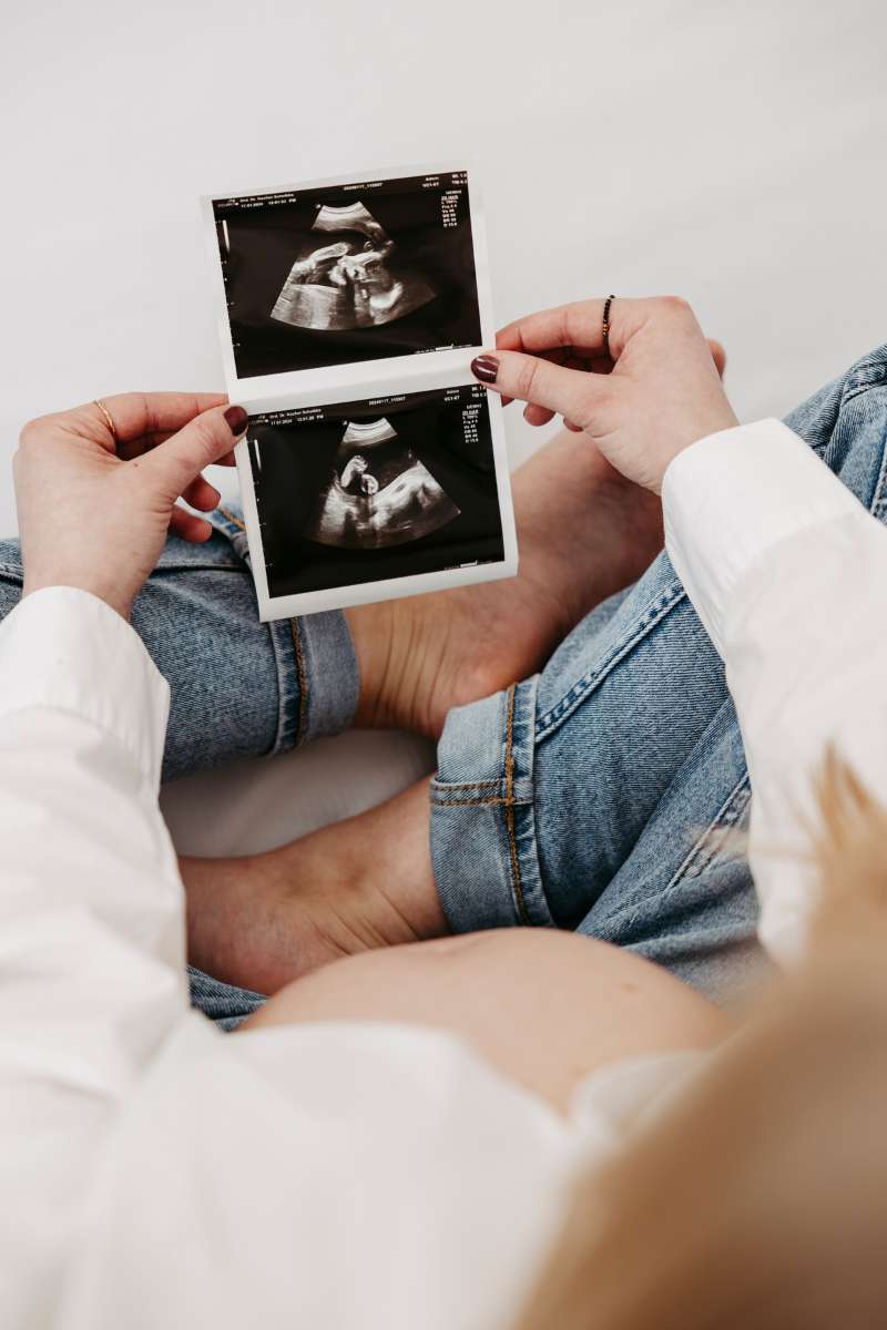 Zwei H&auml;nde halten Ultraschallbilder &uuml;ber einem Babybauch
