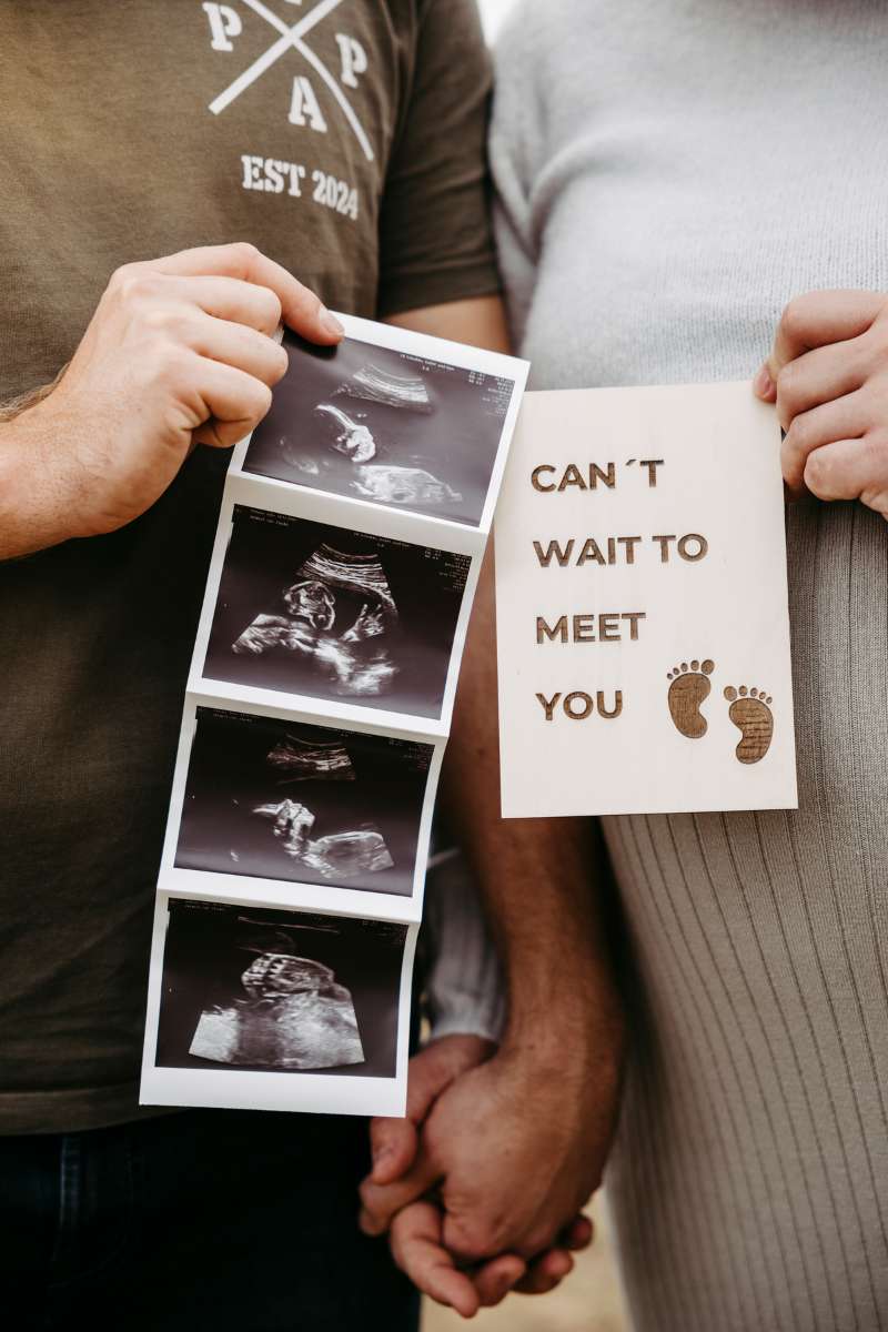 Werdende Eltern halten Ultraschallbilder und eine Karte mit der Aufschrift Can&rsquo;t wait to meet you