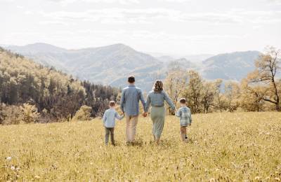 Familie mit zwei Kindern geht Hand in Hand &uuml;ber eine Fr&uuml;hlingswiese