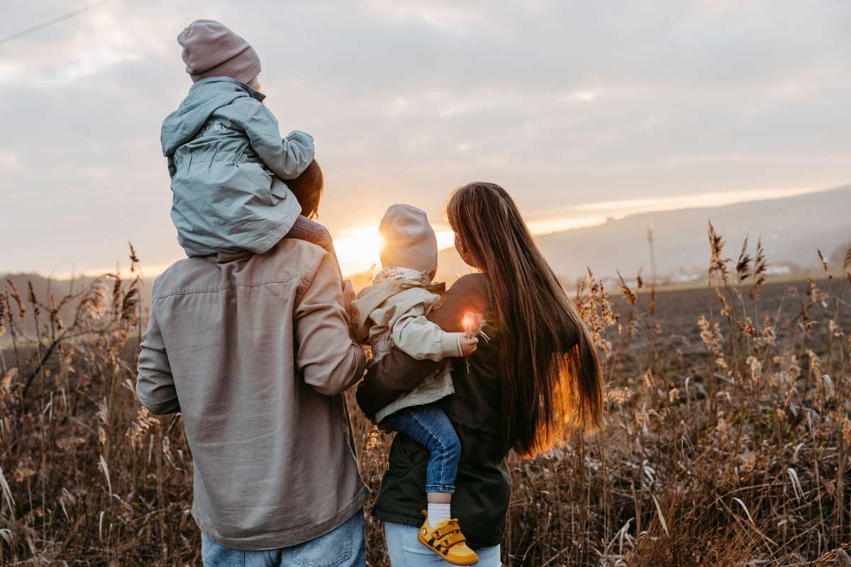 Vater tr&auml;gt ein Kind auf den Schultern, daneben die Mutter mit dem zweiten Kind im Gegenlicht