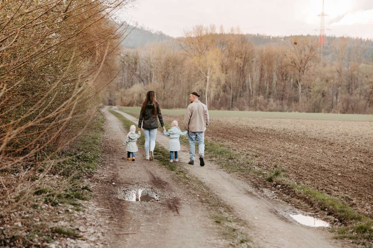 Familie mit zwei kleinen Kindern geht Hand in Hand einen Feldweg entlang