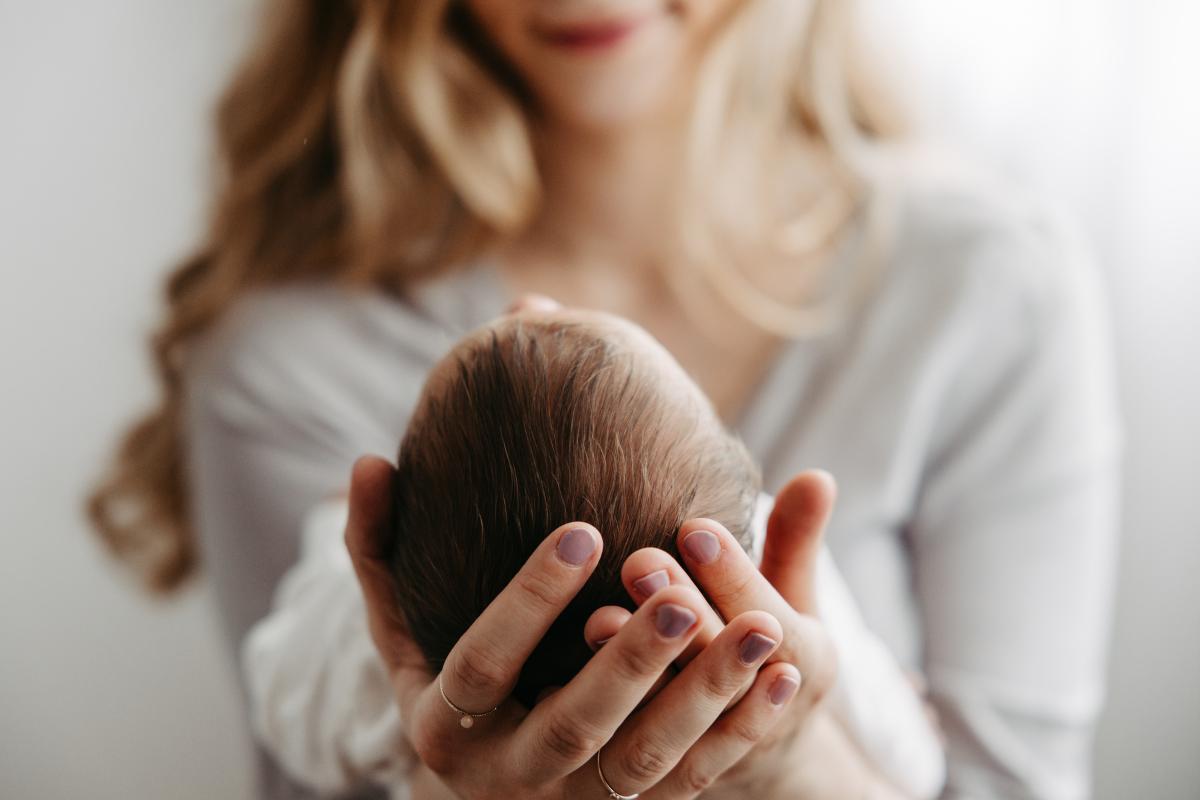 Mutter h&auml;lt den Kopf ihres Neugeborenen in beiden H&auml;nden
