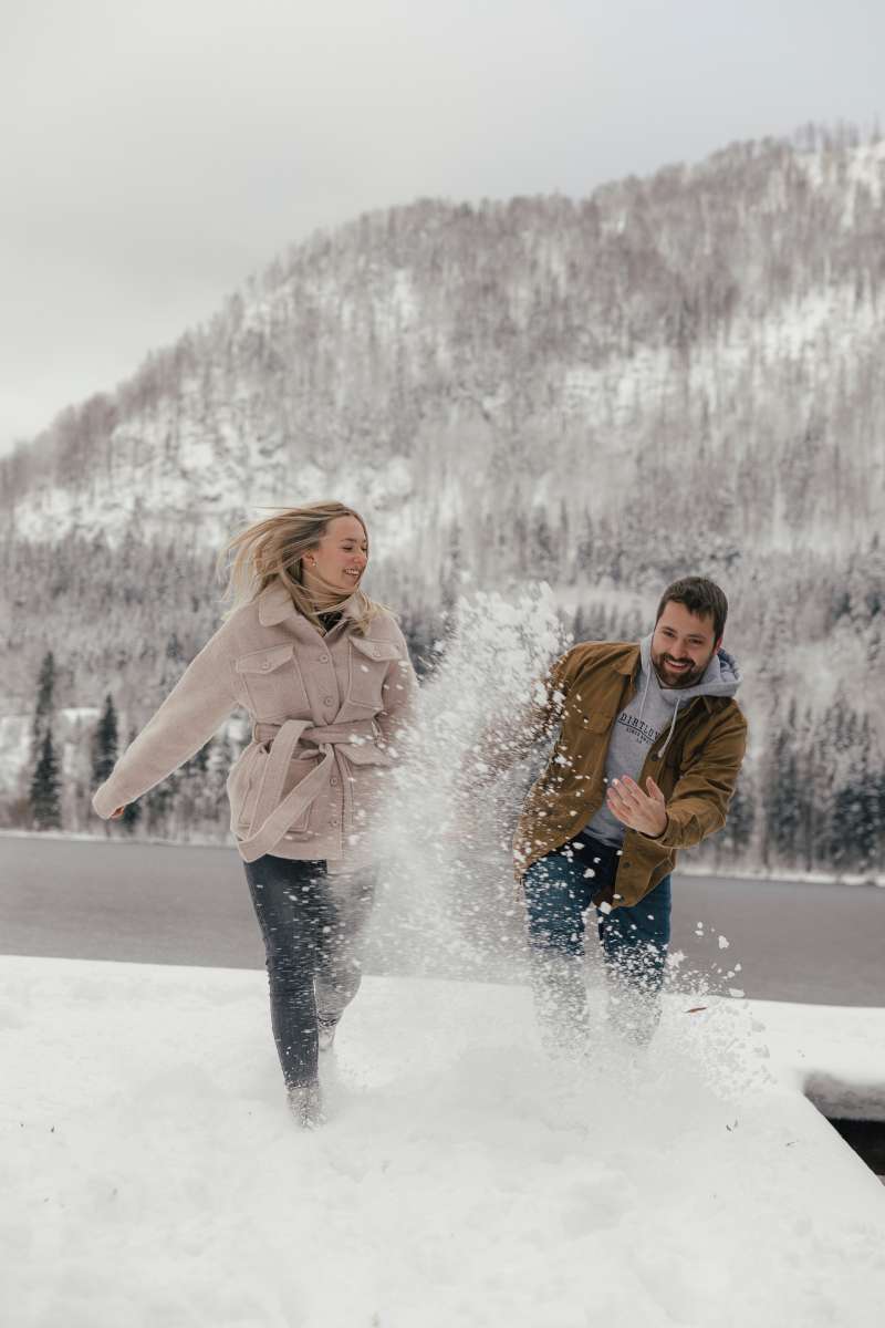 Paar wirft sich vor verschneiten Bergen lachend Schnee zu