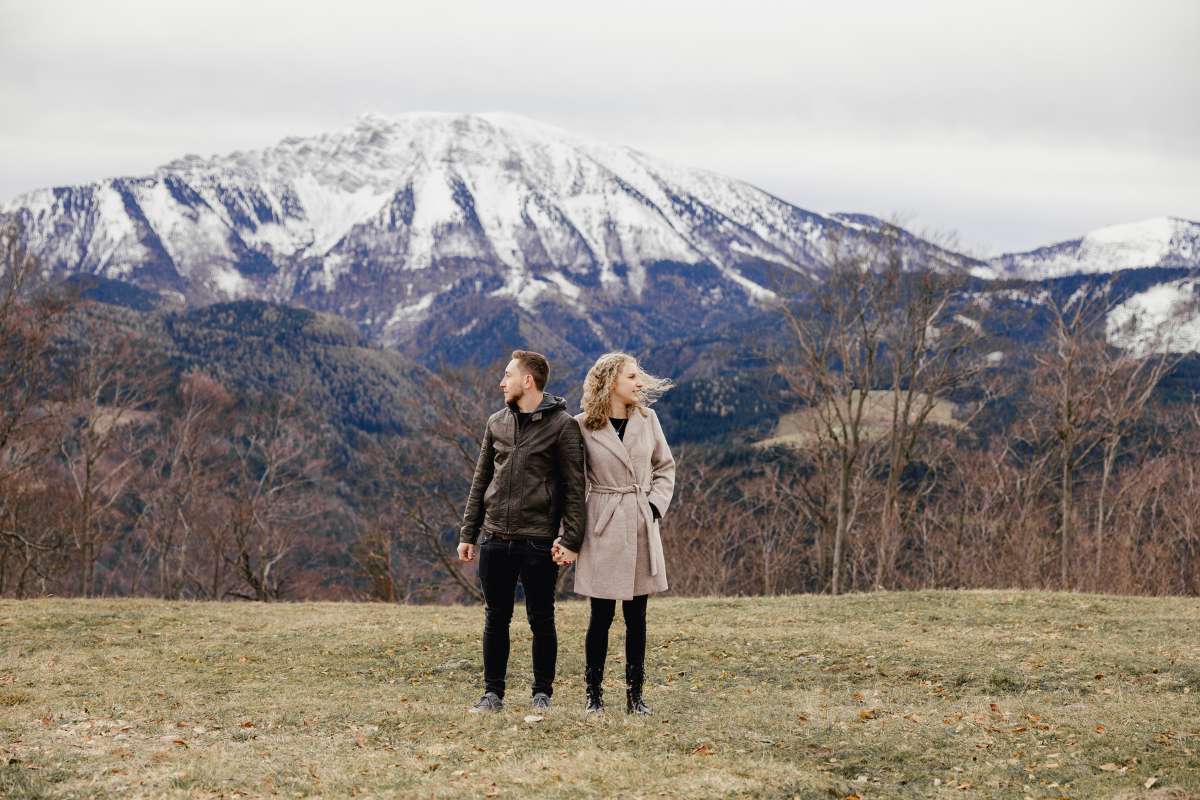 Paar steht klein auf einer Wiese vor einem schneebedeckten Bergmassiv